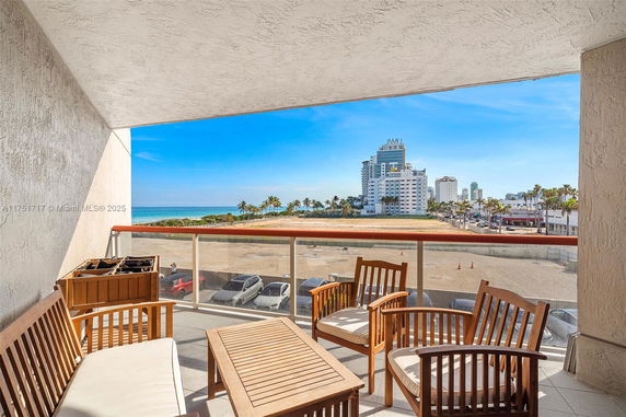 Balcony view overlooking a beach and cityscape with furniture present.
