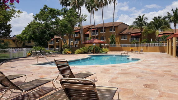 Outdoor swimming pool area surrounded by residential buildings and palm trees.