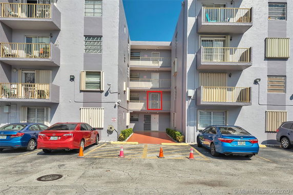 Parking area in front of a multi-story apartment building with balconies.