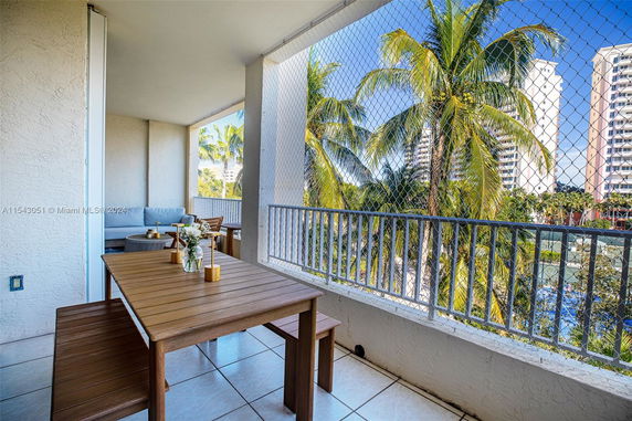 Balcony view from an apartment with outdoor seating, overlooking palm trees and nearby buildings.