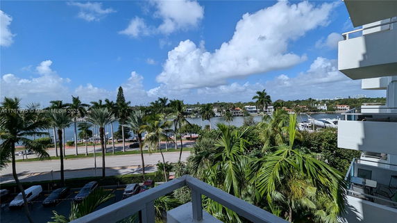 View of palm trees, a road, and water with houses in the distance from a building.