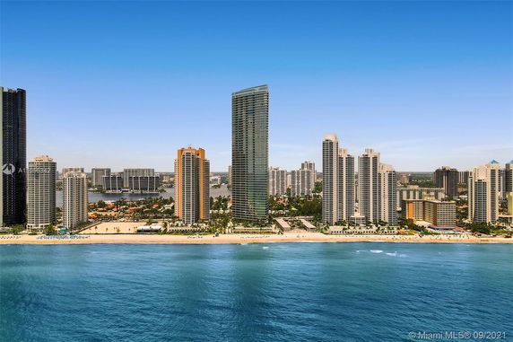 Aerial view of tall buildings along the coastline with a beach in the foreground.