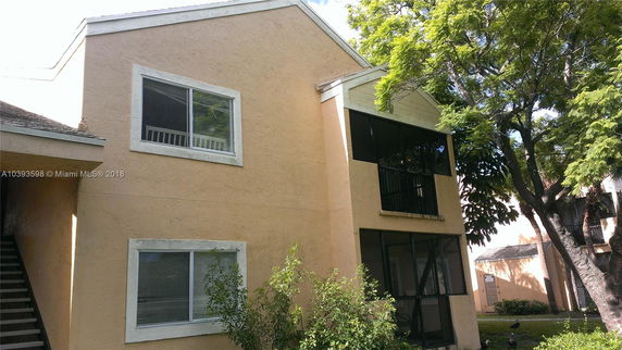 Front view of a two-story building with beige stucco walls and screened balcony.
