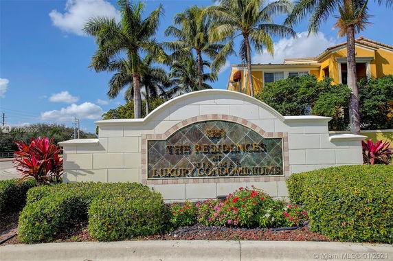 Entrance sign for luxury condominiums with palm trees and building in the background.