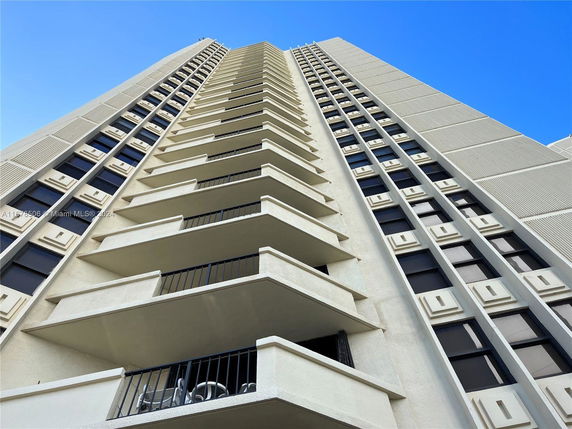 Upward view of a tall building with multiple balconies and grid-like window design.