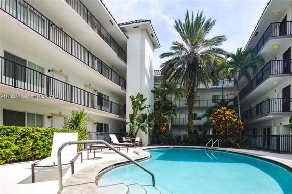 Outdoor view of a multi-story building with a swimming pool surrounded by balconies and palm trees.