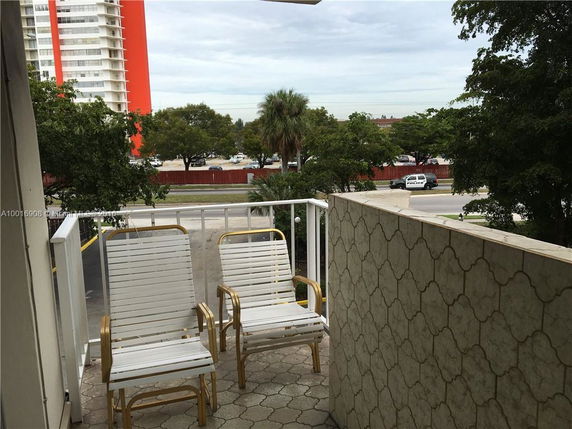 Balcony view with two white chairs overlooking a street and nearby buildings.