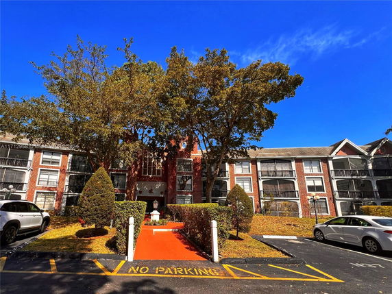 Front view of a multi-story brick apartment building with parking area.