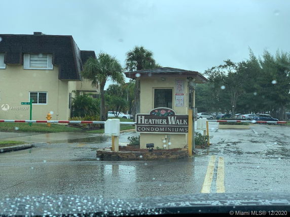 Front view of a condominium complex entrance with a guardhouse and sign.