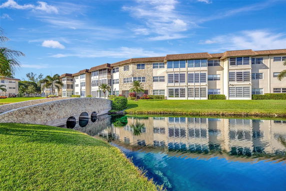 Front view of a multi-story residential complex with a stone bridge crossing a small water body.