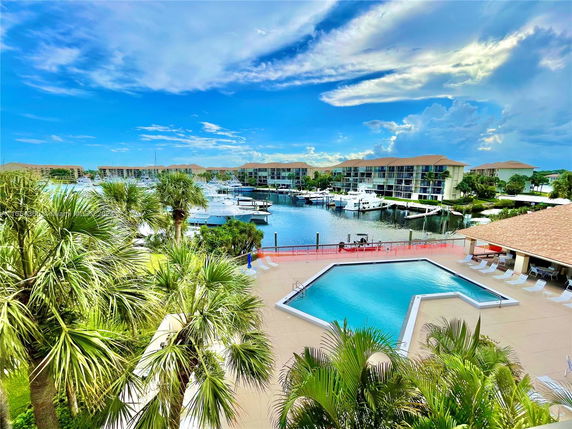View of waterfront buildings and a marina with palm trees and a swimming pool in the foreground.