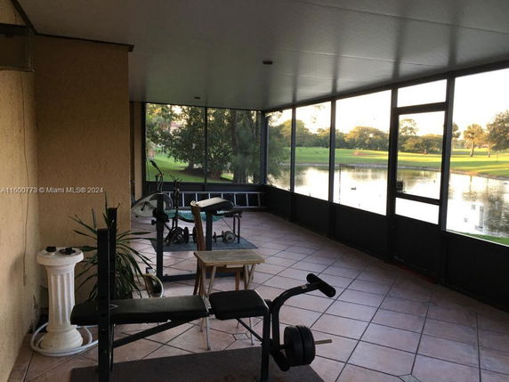 Indoor gym area with exercise equipment and view of a pond through large windows.