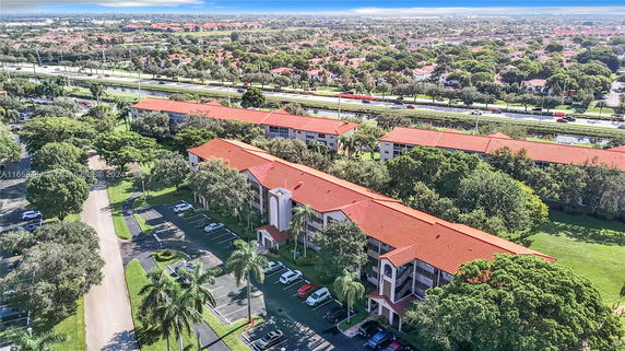 Aerial view of a residential complex with red-tiled roofs surrounded by greenery and roads.