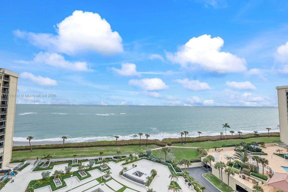 Panoramic view of the ocean and coastline from a building, with landscaped areas and palm trees.