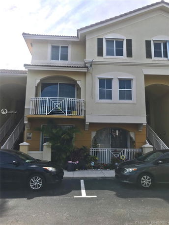 Front view of a two-story residential building with balconies and parked cars.