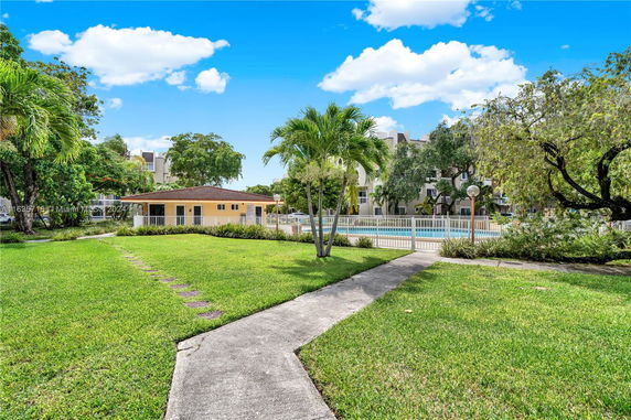 View of a building with a fence and a swimming pool in front, surrounded by greenery and trees.