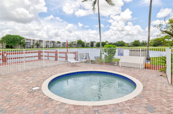 Outdoor swimming pool with a circular design and fenced surroundings near a water body.