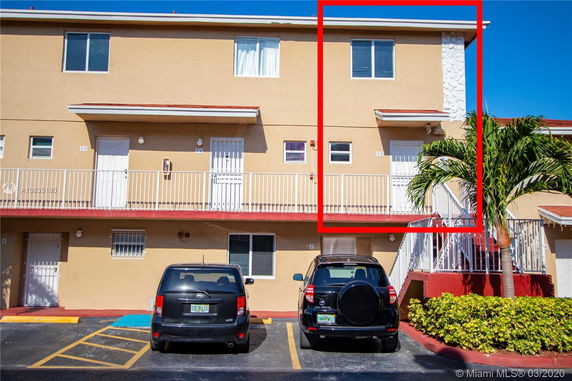 Front view of a multi-story building with a balcony and parking area.