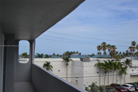 View from a building balcony overlooking a parking area and distant ocean.
