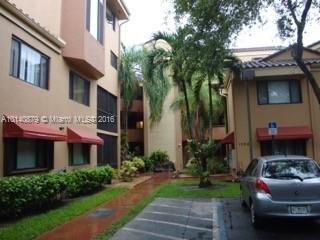 View of a multi-story residential building with red awnings and adjacent parking area.