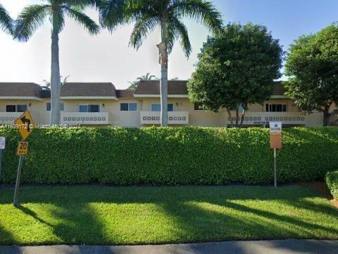 Front view of a single-story building with a hedge and palm trees.