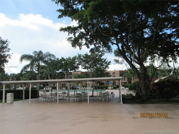 Outdoor area with covered seating and a view of a swimming pool surrounded by trees.