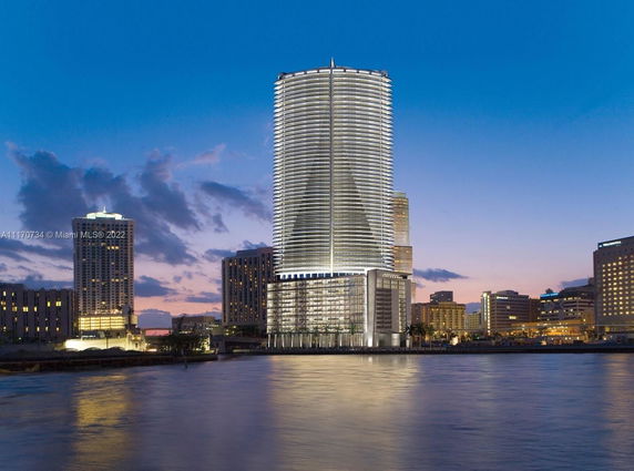 Front view of a modern high-rise building by the water at dusk.