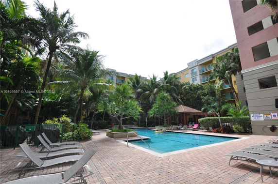 View of apartment buildings surrounding a swimming pool with lounge chairs and palm trees.