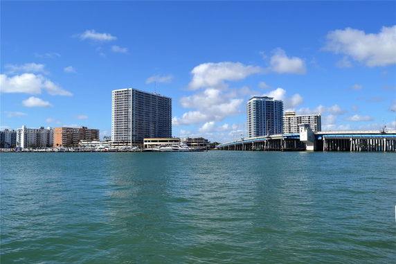 Distant view of multiple high-rise buildings near a body of water with a bridge extending across the water.