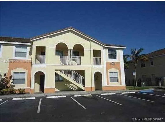 Front view of a two-story apartment building with arched upper balconies and external staircase.