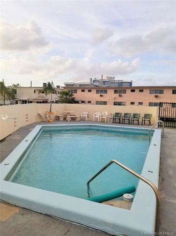 Rectangular outdoor swimming pool on a rooftop with chairs and a view of nearby buildings.