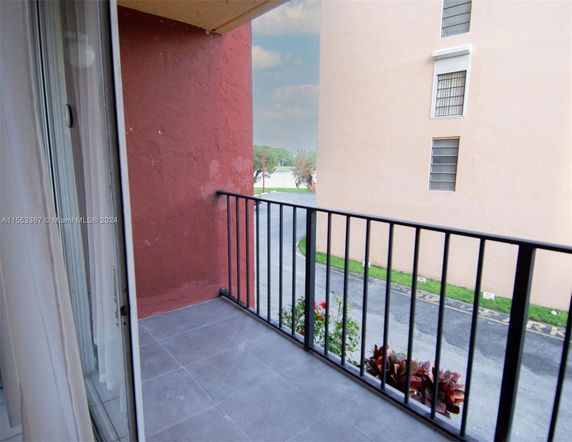 View from a balcony with railing overlooking a parking area and adjacent building.