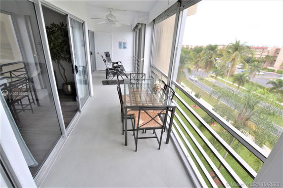Balcony view with glass table and chairs, overlooking a landscaped area and palm trees.