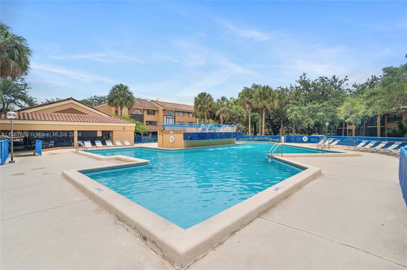 Outdoor swimming pool area with surrounding buildings and palm trees.
