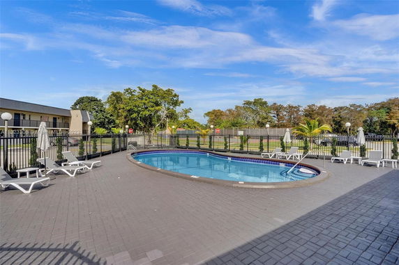Outdoor swimming pool area with lounge chairs and surrounding fence.