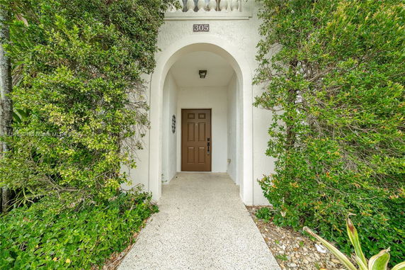 Front entrance of a house with an archway and a brown door, surrounded by greenery.