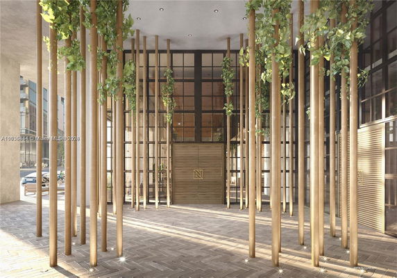 Front view of a modern building entrance with tall vertical wooden pillars and greenery.