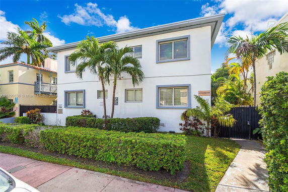 Front view of a two-story house with white exterior and palm trees.