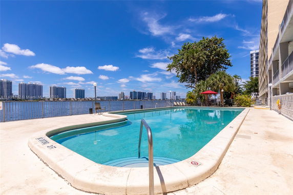 Outdoor swimming pool with water view and high-rise buildings in the background.