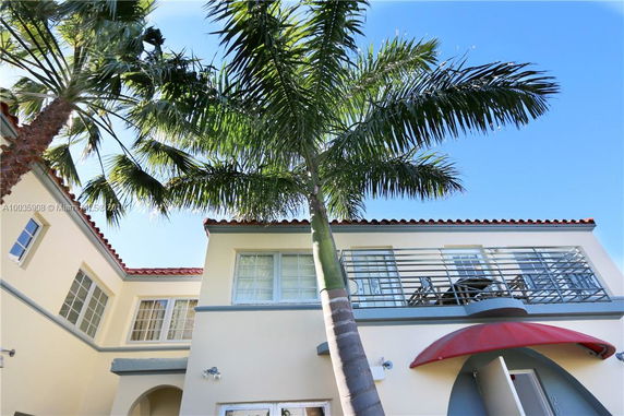 Front view of a two-story house with a balcony and palm trees.