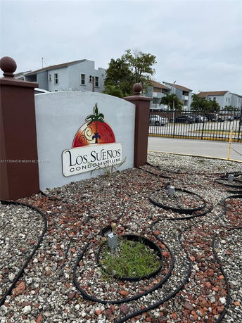 Front view of a condominium entrance sign with buildings in the background.