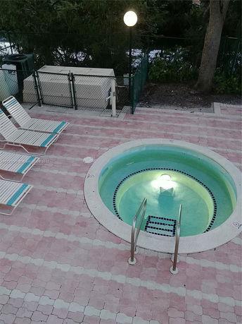 View of a circular outdoor hot tub with a tile surround and nearby lounge chairs.