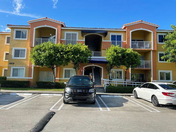 Front view of a three-story apartment building with balconies and parking area.
