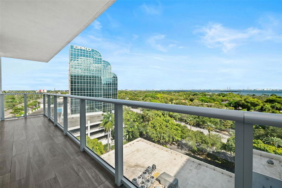 Balcony view overlooking a cityscape with a prominent glass building and greenery.