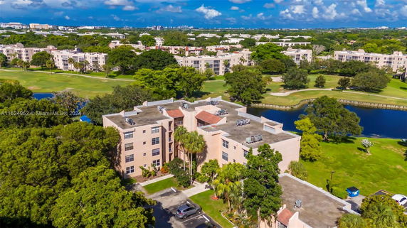 Aerial view of a multi-story building surrounded by trees and greenery with a water body nearby.
