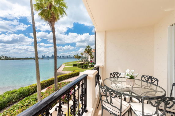 A balcony with a table and chairs overlooking a body of water and city skyline.