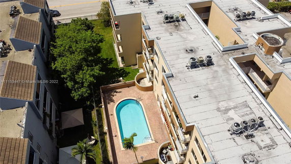 Aerial view of a building with a flat rooftop featuring multiple air conditioning units and a swimming pool area on the ground level.