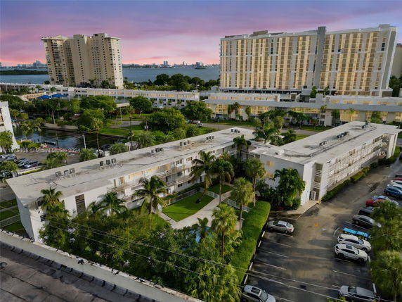 View of apartment buildings with surrounding greenery and parked cars.
