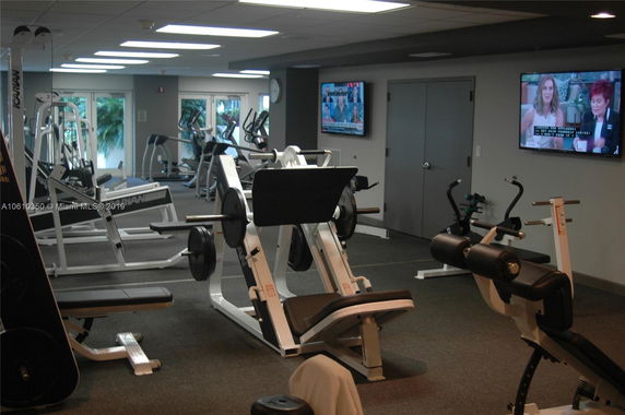Indoor gym area with various exercise equipment and wall-mounted televisions.