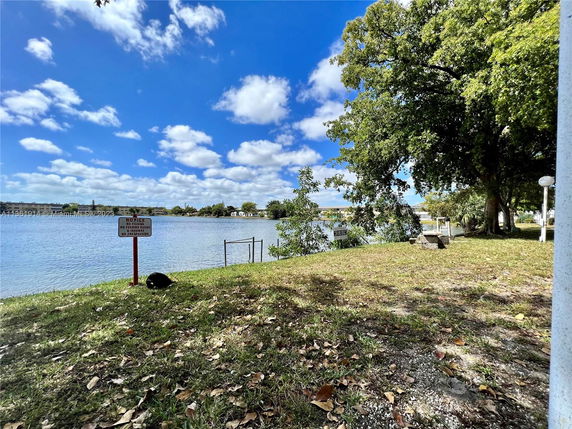 View of a lake with trees and a grassy area, and a notice sign by the water.